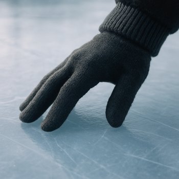 Рука в перчатке касается прозрачного льда с тонкими трещинами