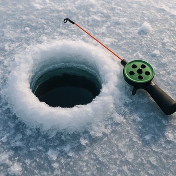 Лунка во льду и удочка для подлёдной рыбалки рядом